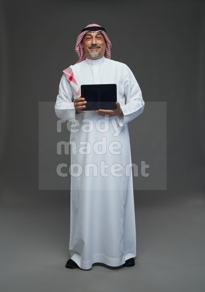 Saudi man with shomag Standing working on tablet on gray background