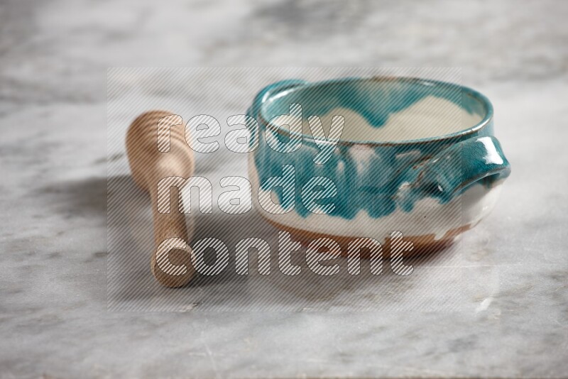 Multicolored pottery bowl with wooden honey dipper on the side on grey marble background
