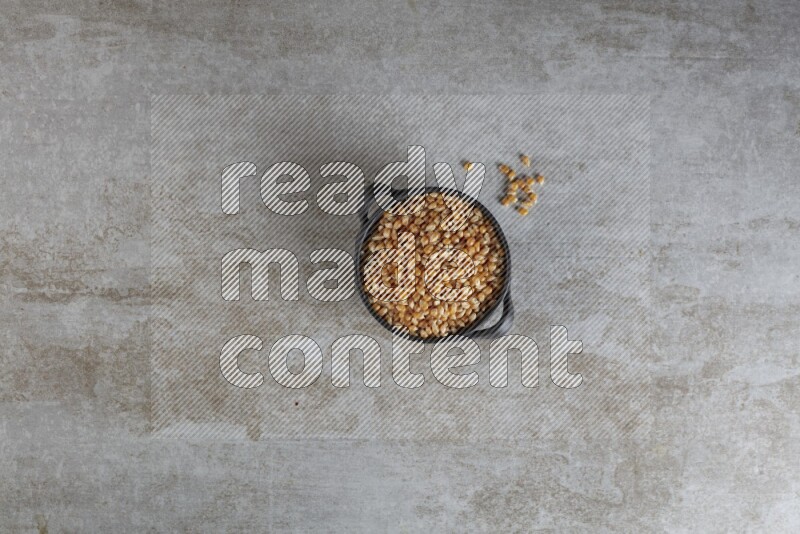 corn kernel in a black handheld ceramic bowl on a grey textured countertop