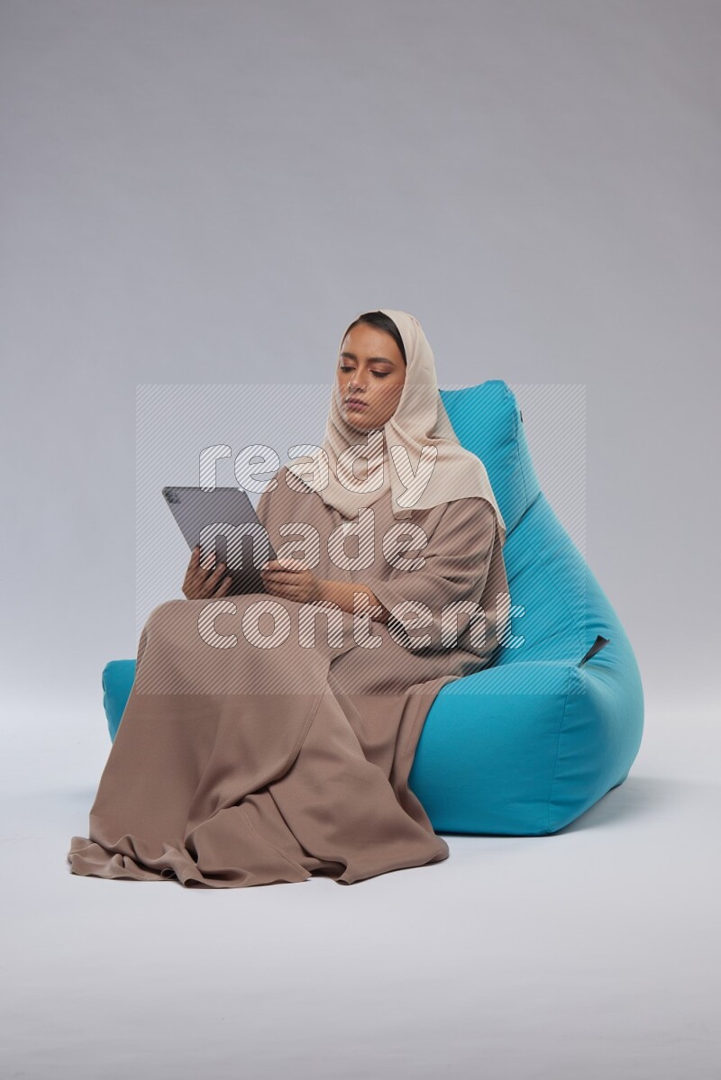 A Saudi woman sitting on a blue beanbag and working on tablet