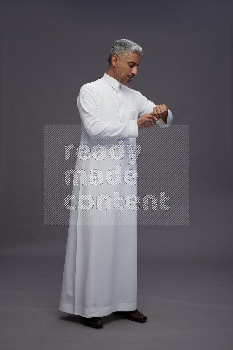 Saudi man wearing thob with neck strap employee badge standing interacting with the camera on gray background