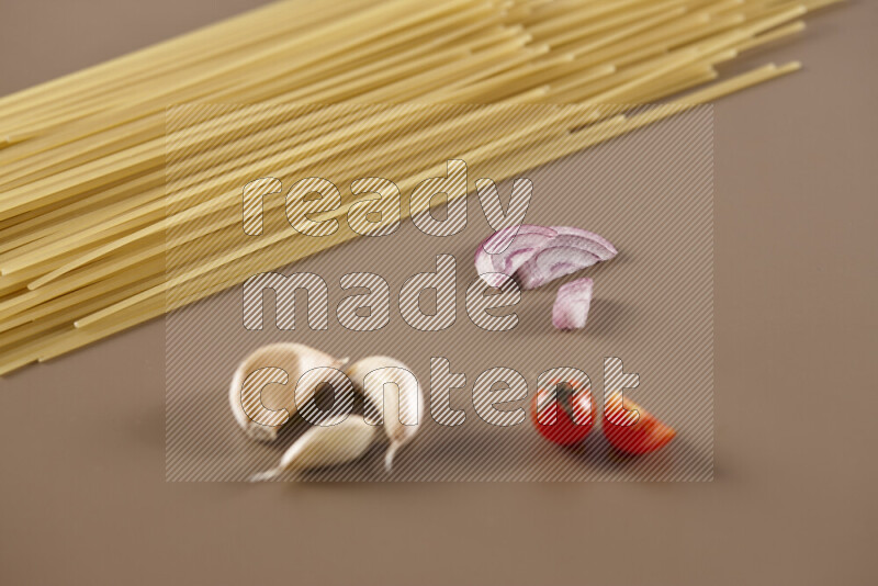 Raw pasta with different ingredients such as cherry tomatoes, garlic, onions, red chilis, black pepper, white pepper, bay laurel leaves, rosemary and cardamom on beige background