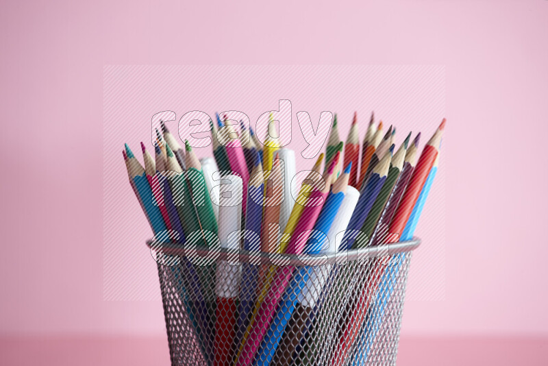 Pens, pencils and other different school supplies in a metal pen holder on rose background
