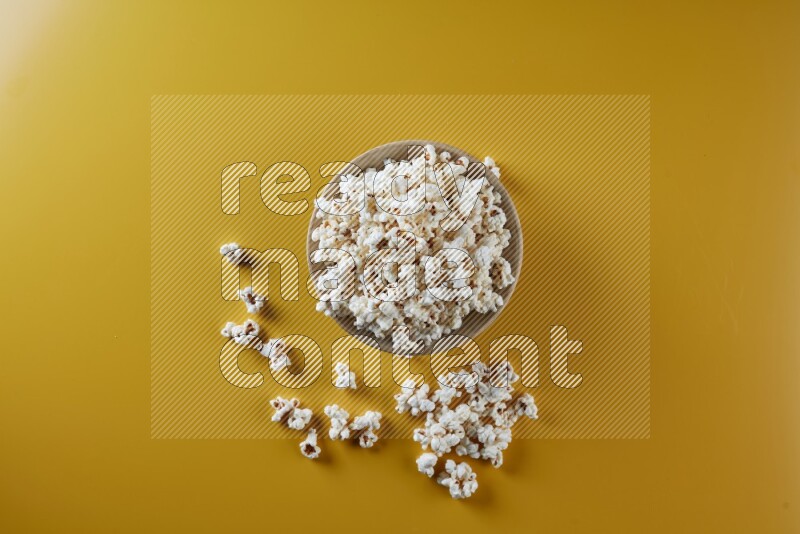 A multicolored ceramic plate full of popcorn with popcorn beside it on a yellow background in different angles