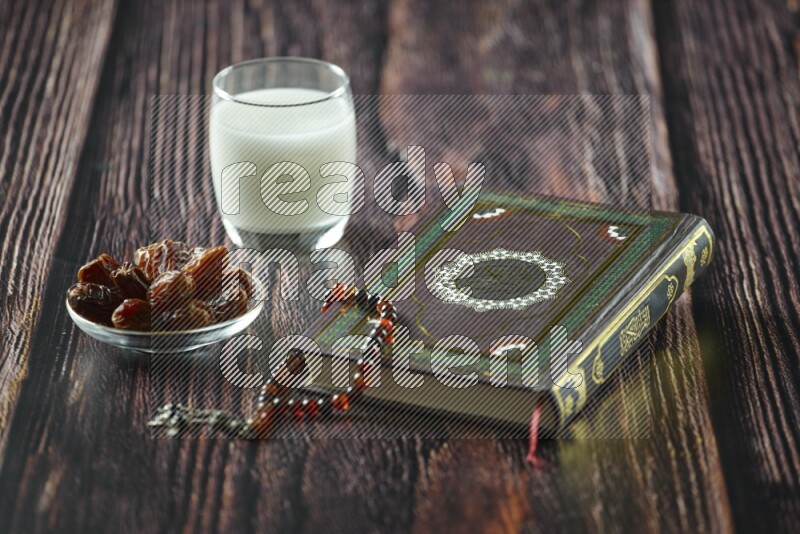 Quran with dates, prayer beads and different drinks all placed on wooden background