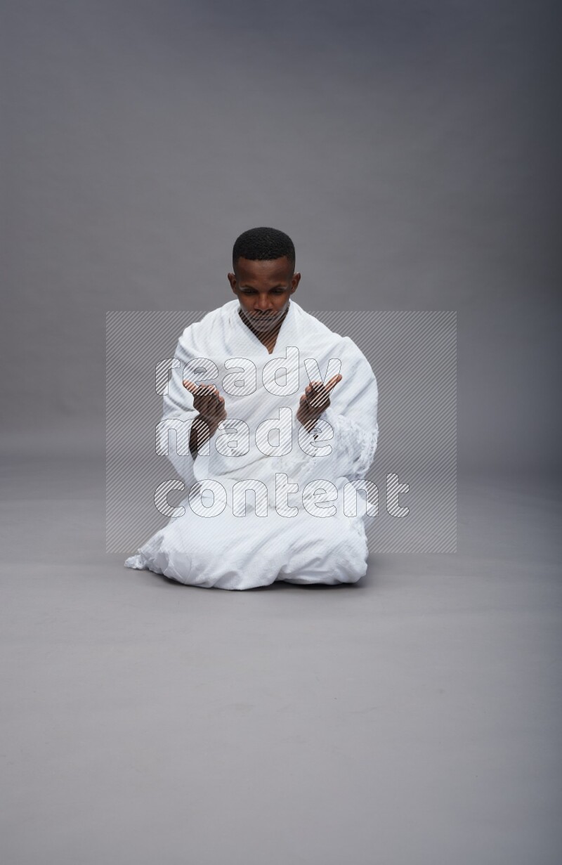 A man wearing Ehram sitting on floor dua'a on gray background