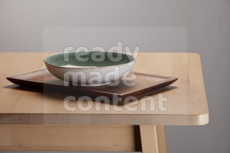 multicolored bowl placed on a rectangular wooden tray on the edge of wooden table
