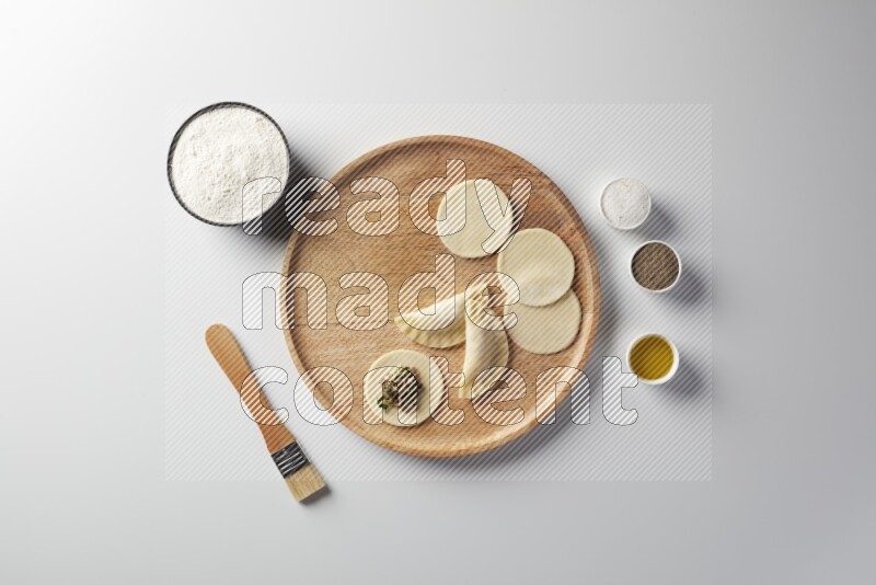 two closed sambosas and one open sambosa filled with meat while flour, salt, black pepper and oil with oil brush aside in a wooden dish on a white background