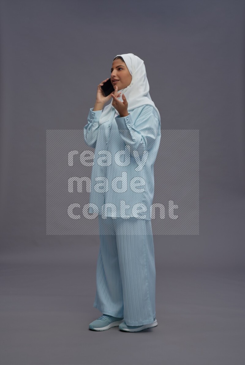 Saudi woman wearing hijab clothes standing talking on phone on gray background