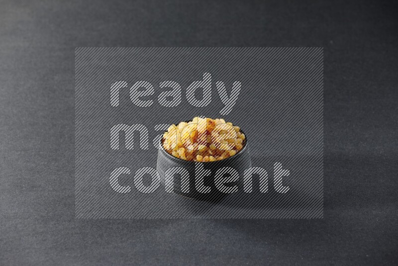 A black pottery bowl full of raisins on a black background in different angles