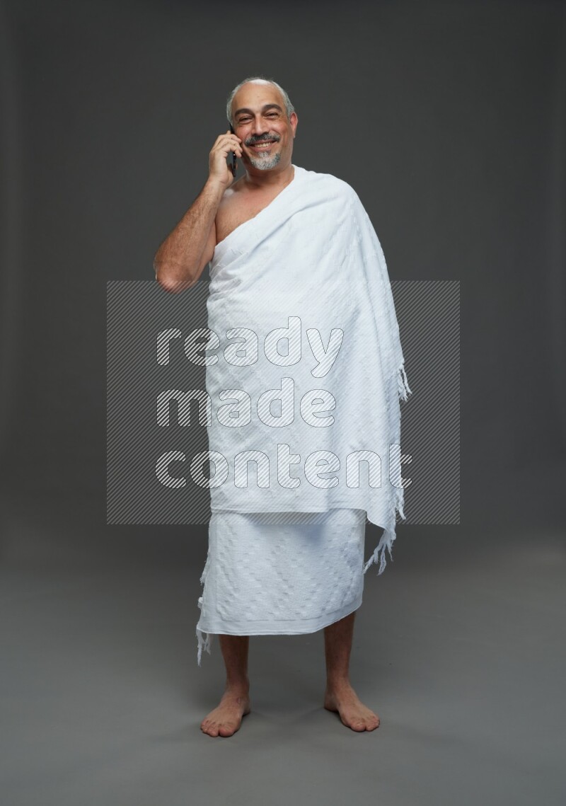 A man wearing Ehram Standing talking on phone on gray background