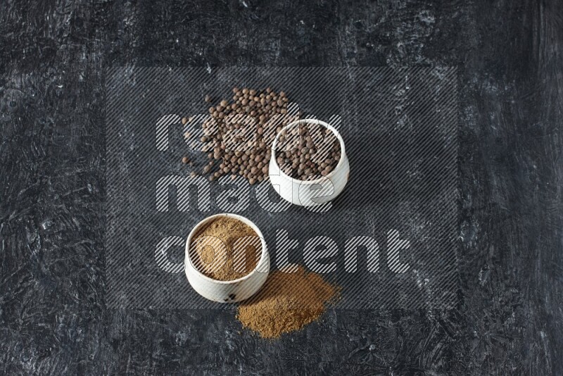 2 beige bowls, one full of allspice powder and the other full of whole balls and both spread on a textured black flooring