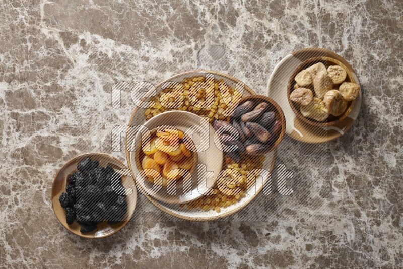 Dried fruits in pottery plates and wooden bowls in a light setup