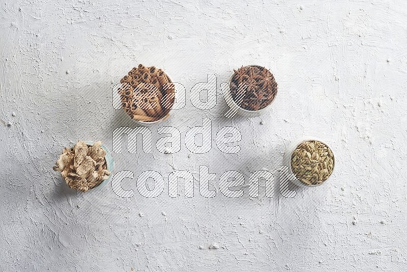Cardamom, ginger, cinnamon sticks and star anise in 4 bowls on a textured white background