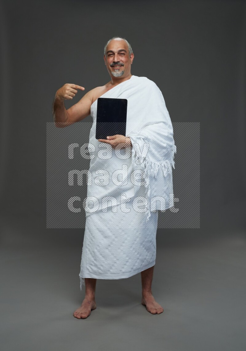 A man wearing Ehram Standing working on tablet on gray background