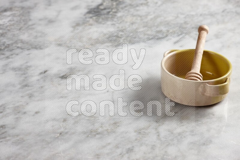 Multicolored pottery bowl with wooden honey dipper in it on grey marble background