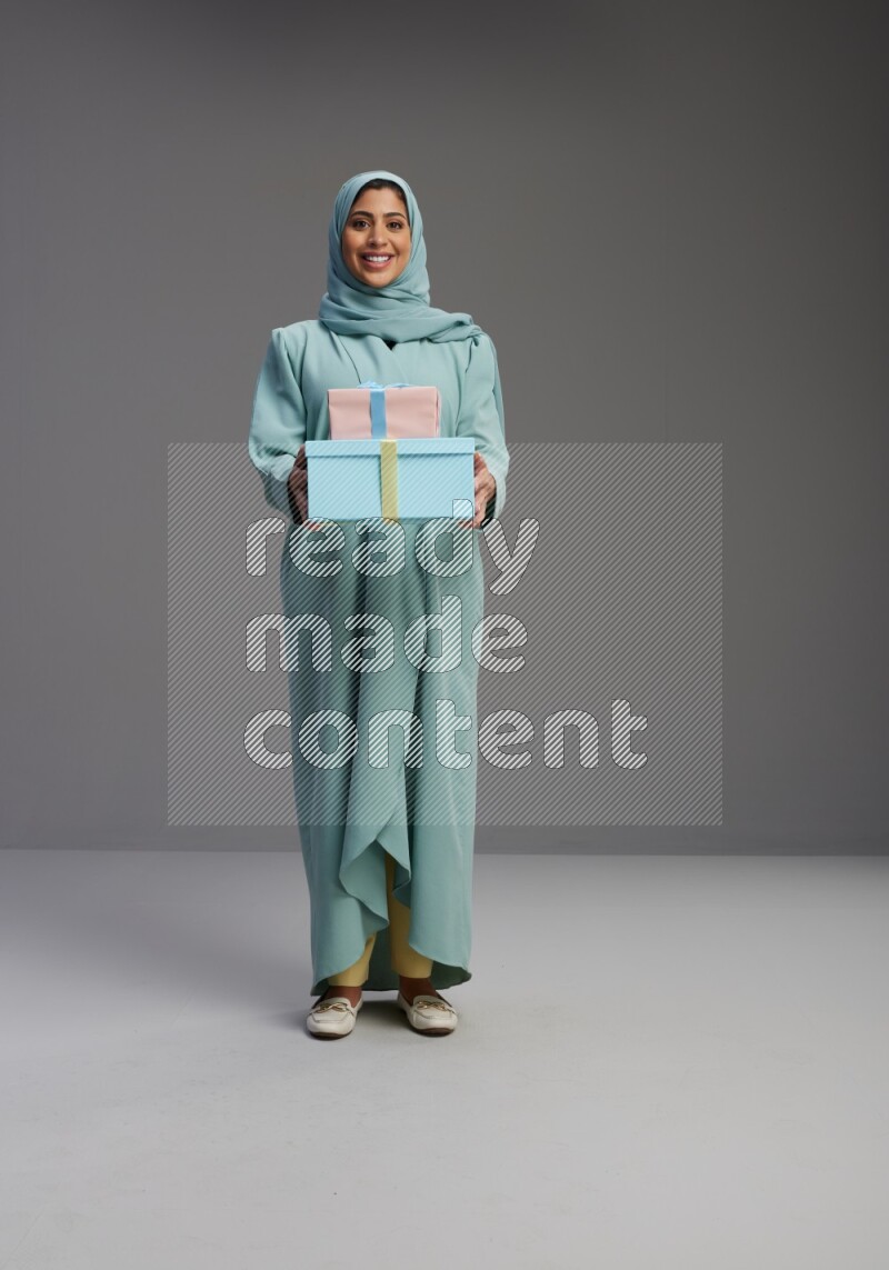 Saudi Woman wearing Abaya standing holding gift box on Gray background