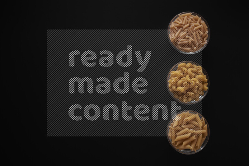 Different pasta types in 3 glass bowls on black background