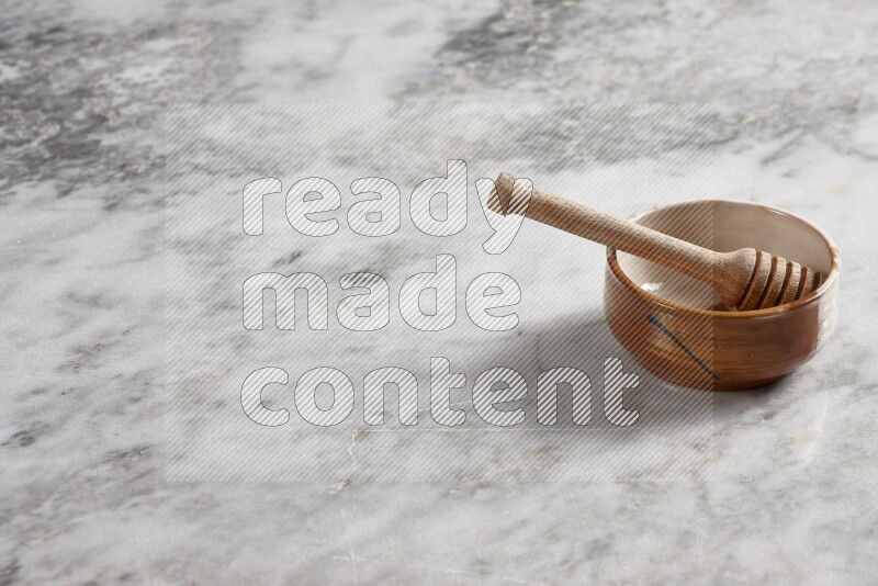 Multicolored pottery bowl with wooden honey dipper in it on grey marble background