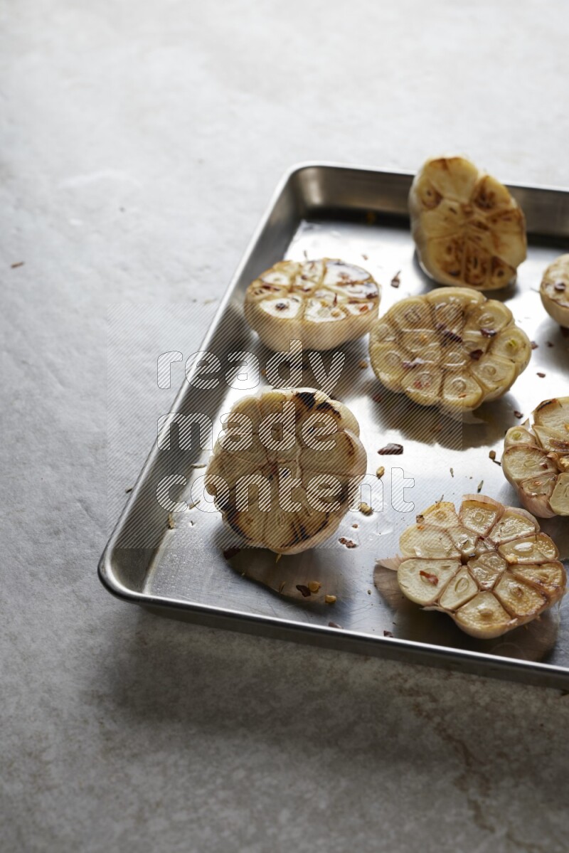 half's roasted garlic in a stainless tray on a grey textured countertop