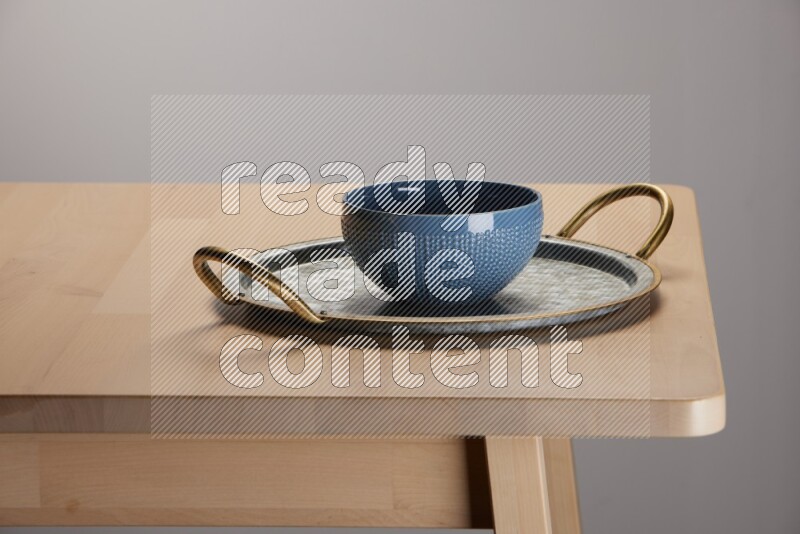 blue bowl placed on a rounded stainless steel metal tray with golden handels on the edge of wooden table