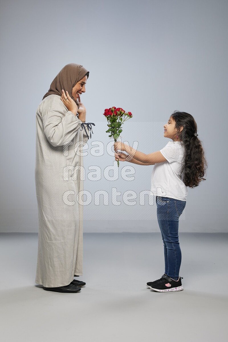 A girl standing giving flowers to her mother on gray background