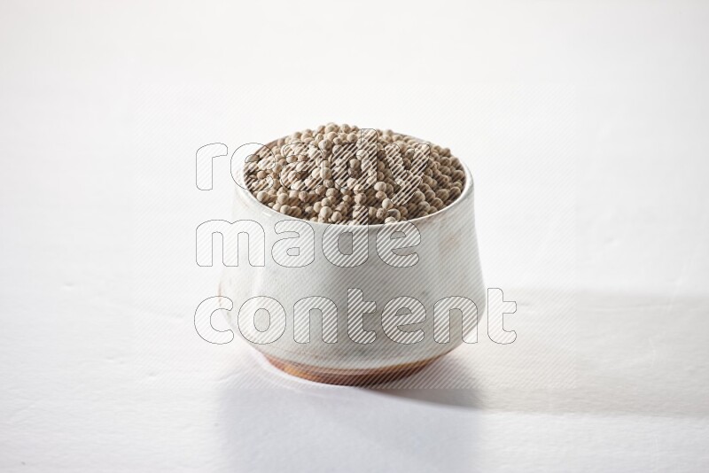 A beige pottery bowl full of white pepper beads on white flooring