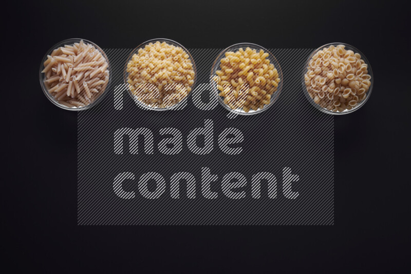 Different pasta types in glass bowls on black background
