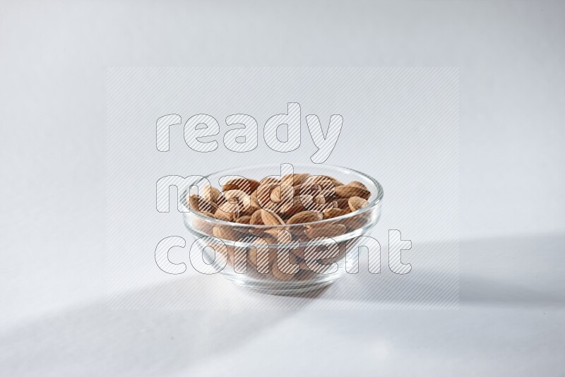 A glass bowl full of peeled almonds on a white background in different angles