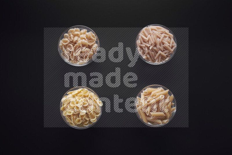 Different pasta types in glass bowls on black background