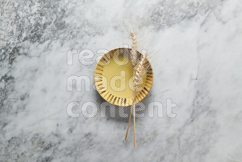 Wheat stalks on multicolored pottery plate on grey marble background