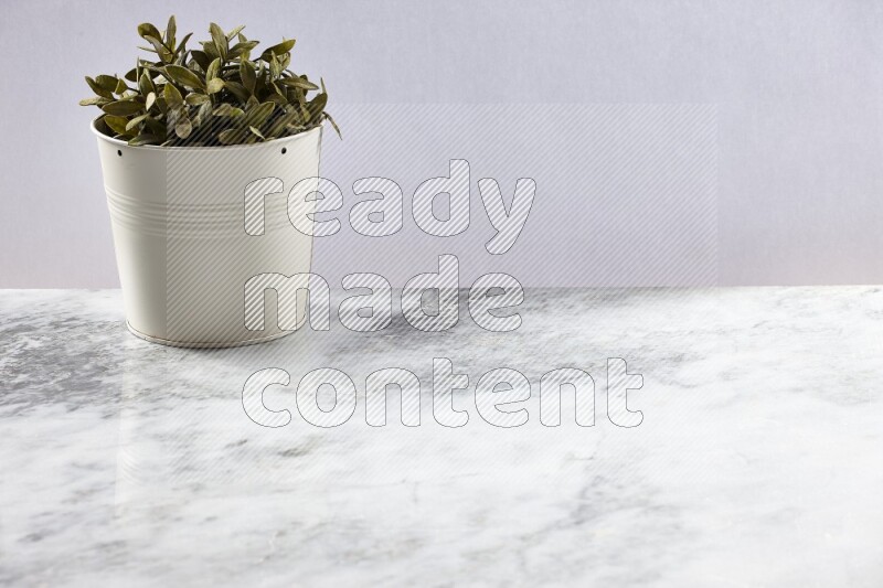 Green artificial plant in white pot on light grey marble background