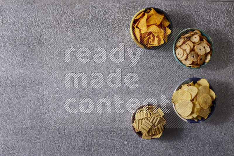 Assorted snacks in pottery bowls on grey background