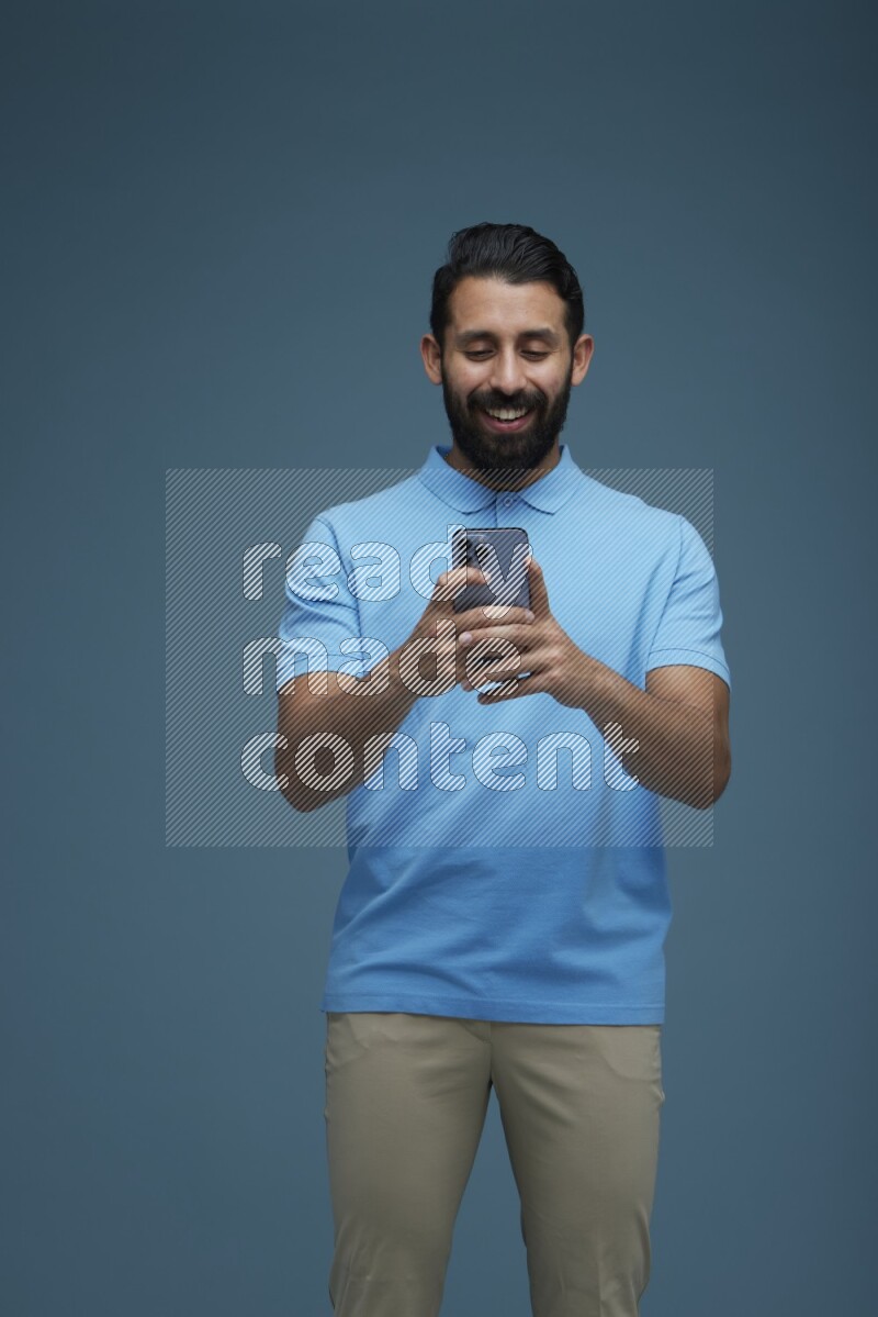 A man Texting on his phone in a blue background wearing a Blue shirt