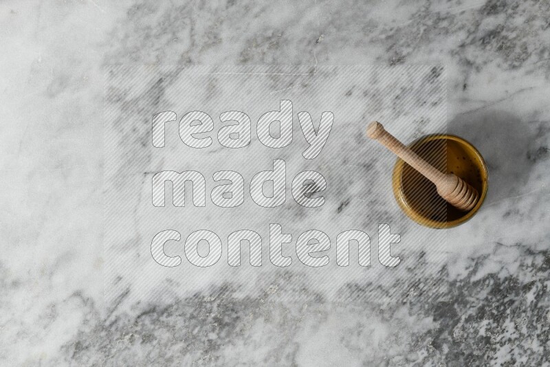 Multicolored pottery bowl with wooden honey dipper in it on grey marble background