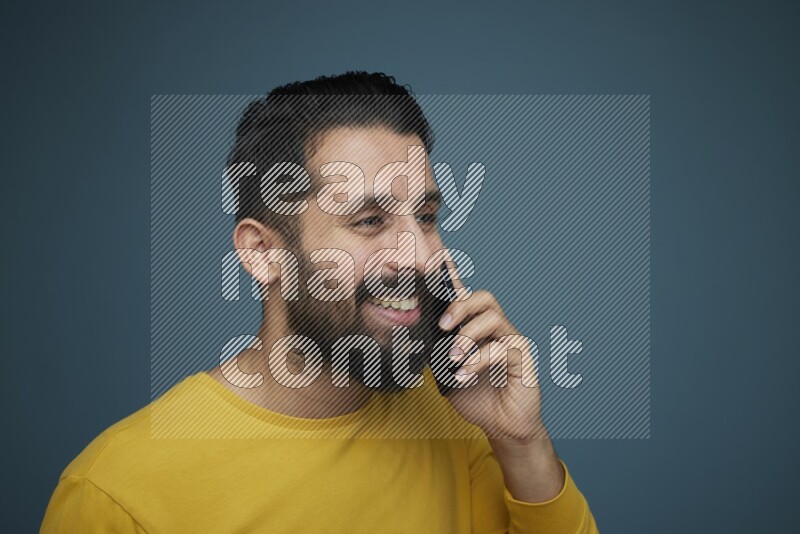 A man having a calling in a blue background wearing a yellow shirt