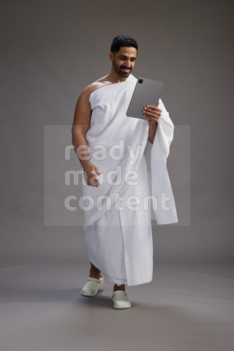 A man wearing Ehram and holding a tablet on gray background