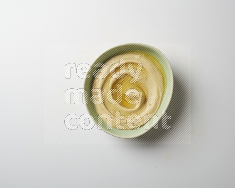 Hummus in a green plate garnished with olive oil on a white background