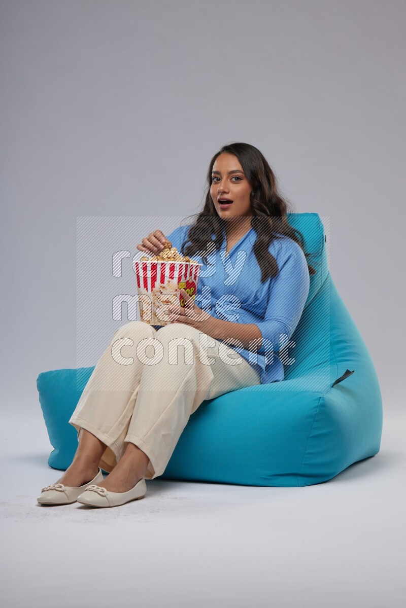 A woman sitting on a blue beanbag and eating popcorn