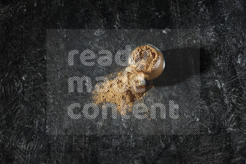 وعاء زجاجي للتوابل مقلوب ممتلئ ببودرة بهار الفلفل الحلو والبودرة تناثرت منه على خلفية سوداء