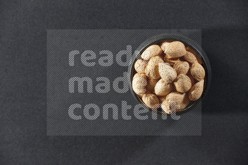 A black pottery bowl full of almonds on a black background in different angles