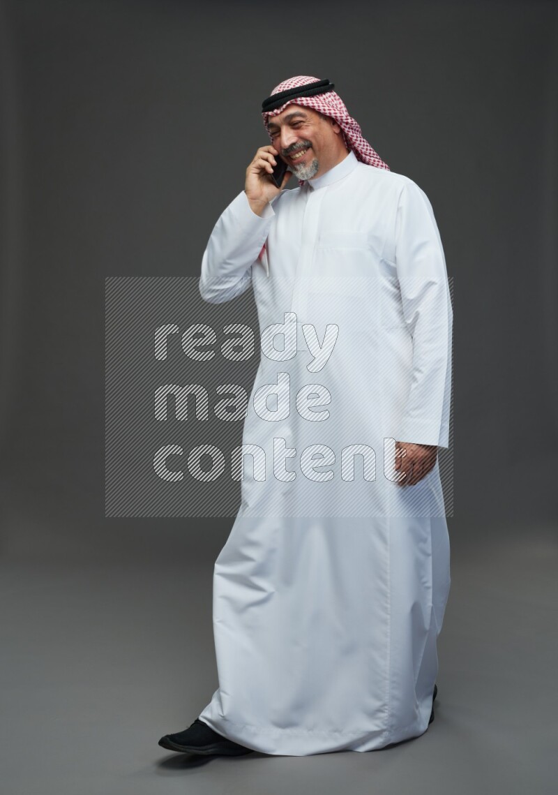 Saudi man with shomag Standing talking on phone on gray background