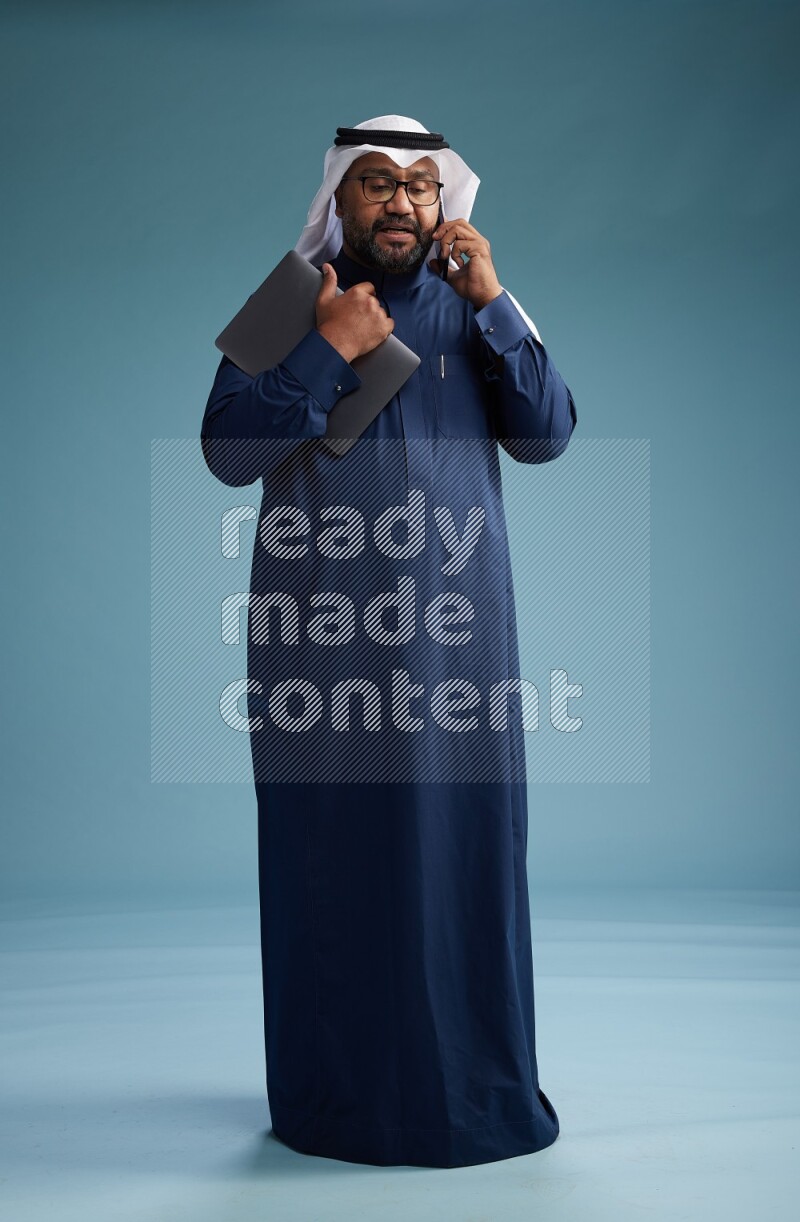 Saudi Man with shimag Standing talking on phone on blue background