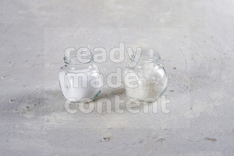 2 glass jars one is filled with table salt and the other with coarse sea salt on white background
