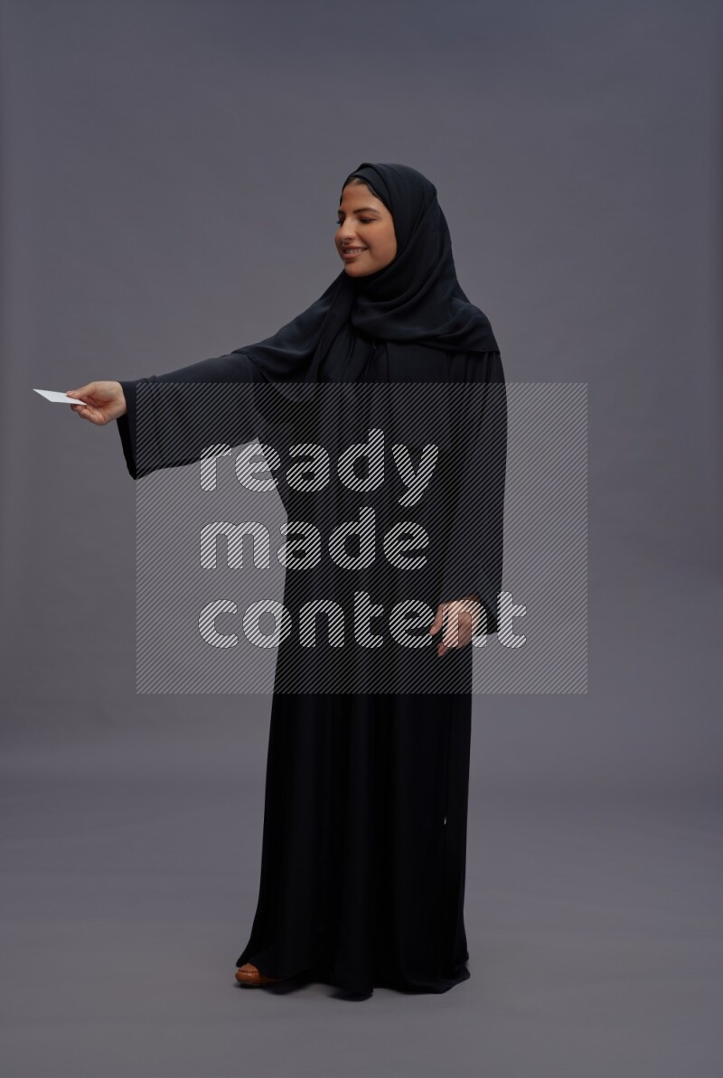 Saudi woman wearing Abaya standing holding ATM card on gray background