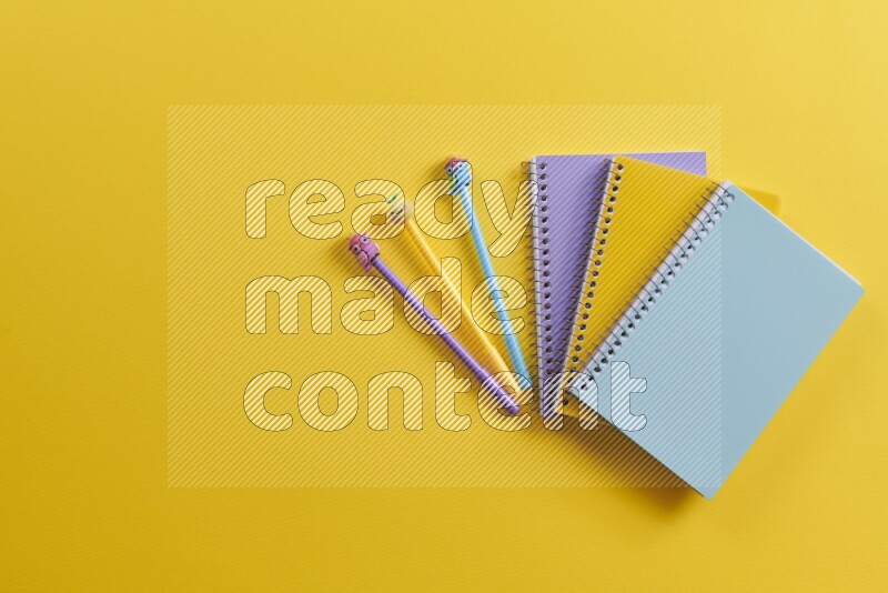 Multicolored notebooks with school supplies on yellow background