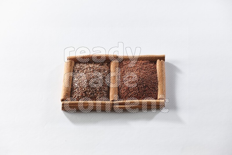 مربعان من أعواد القرفة ممتلئان ببذور الكتان وحب الرشاد علي خلفية بيضاء