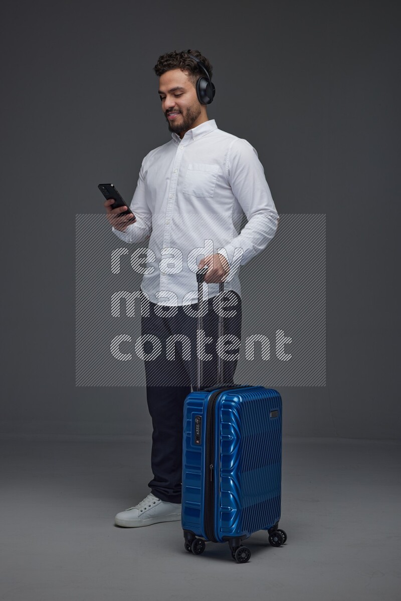 A man wearing smart casual and headphone holding luggage eye level on a gray background