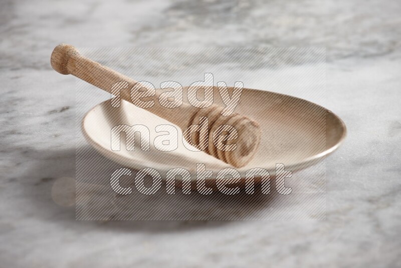 Beige pottery plate with wooden honey dipper in it on grey marble background