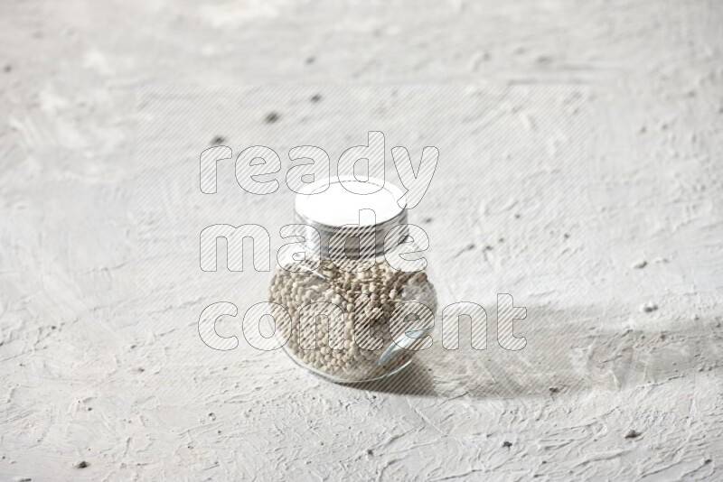Herbal Glass jar full of white pepper beads on textured white flooring